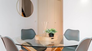 Un espace repas moderne avec une table en verre, deux chaises, une plante en pot et un miroir au mur.