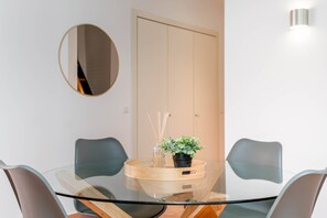 Ein moderner Essbereich mit Glastisch, zwei Stühlen, einer Zimmerpflanze und einem Spiegel an der Wand.