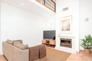 Een woonkamer met een bank, een flatscreen televisie, een open haard en een ingelijst schilderij aan de muur.