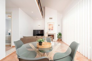 Ein modernes Wohnzimmer mit einem Glastisch, Sofas, einem Fernseher und einem Kamin.