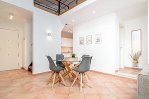 Een eethoek met een glazen tafel en stoelen, een keuken op de achtergrond, en een trap naar een hoger niveau.