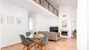 Un salon moderne avec une table à manger en verre, des chaises grises, un canapé, un téléviseur et une cheminée.