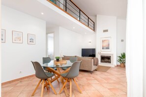 Ein modernes Wohnzimmer mit einem Glastisch, grauen Stühlen, einer Couch, einem Fernseher und einem Kamin.