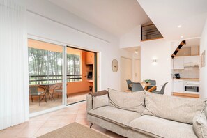 Een moderne woonkamer met een bank, een eettafel met stoelen, een keukenhoek en een glazen schuifdeur die uitkomt op een terras.