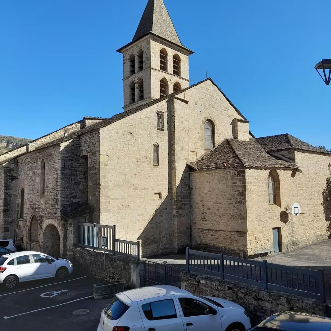 Un bâtiment historique en pierre, doté d’un clocher, d’un parking et surplombant un ciel d’un bleu limpide.