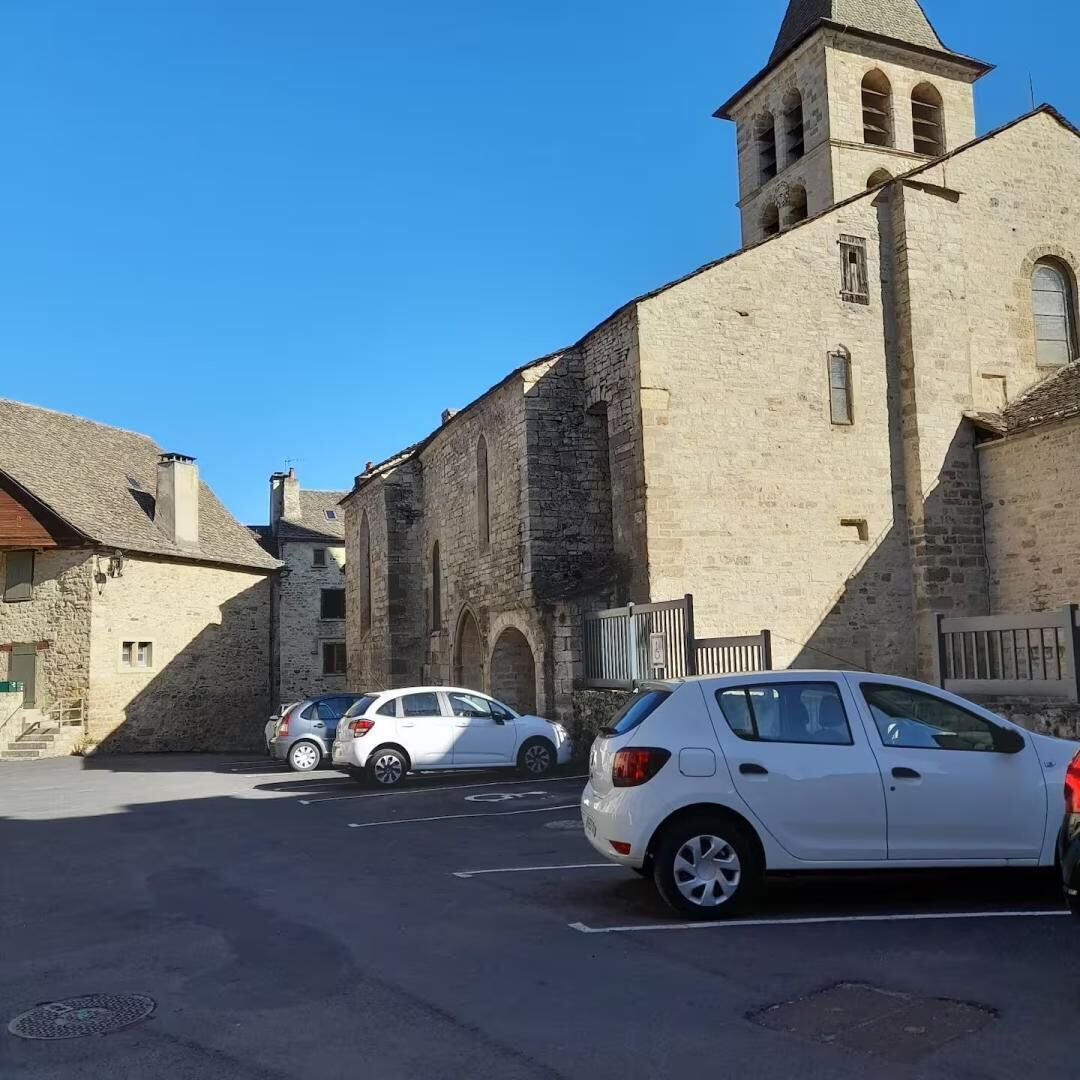 Un edificio histórico de piedra con una torre de campanas, coches aparcados y un cielo azul despejado.