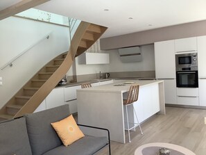 A modern kitchen with a central island, built-in appliances, and a staircase. - La Maisonnette de Colette (CHASTEL-NOUVEL)