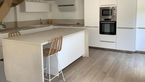 Et moderne køkken med hvide skabe, ovn og en stor ø med en barstol.