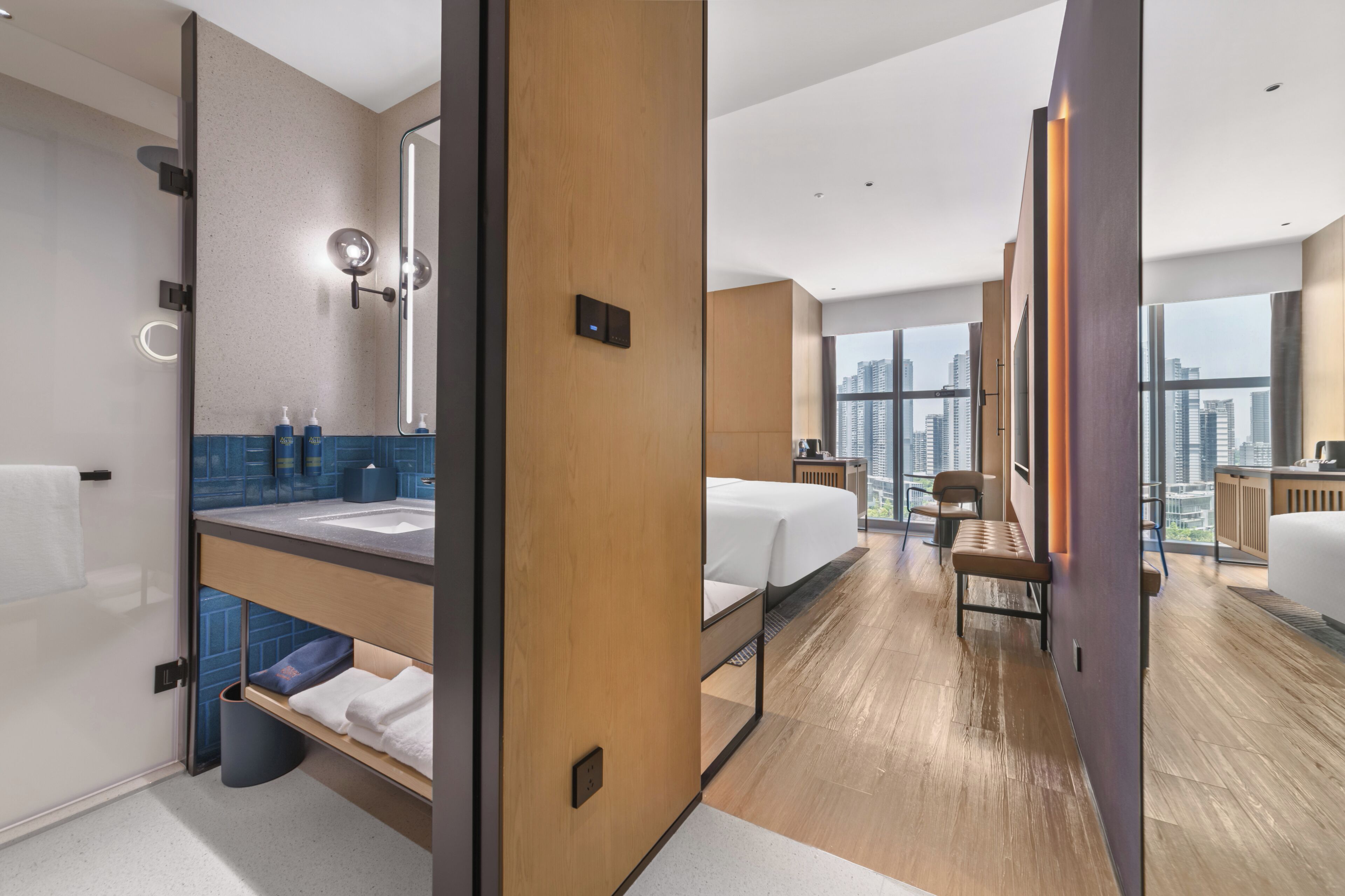 Habitación de hotel moderna con una cama grande, un baño con espejo y lavamanos, y vistas a la ciudad.