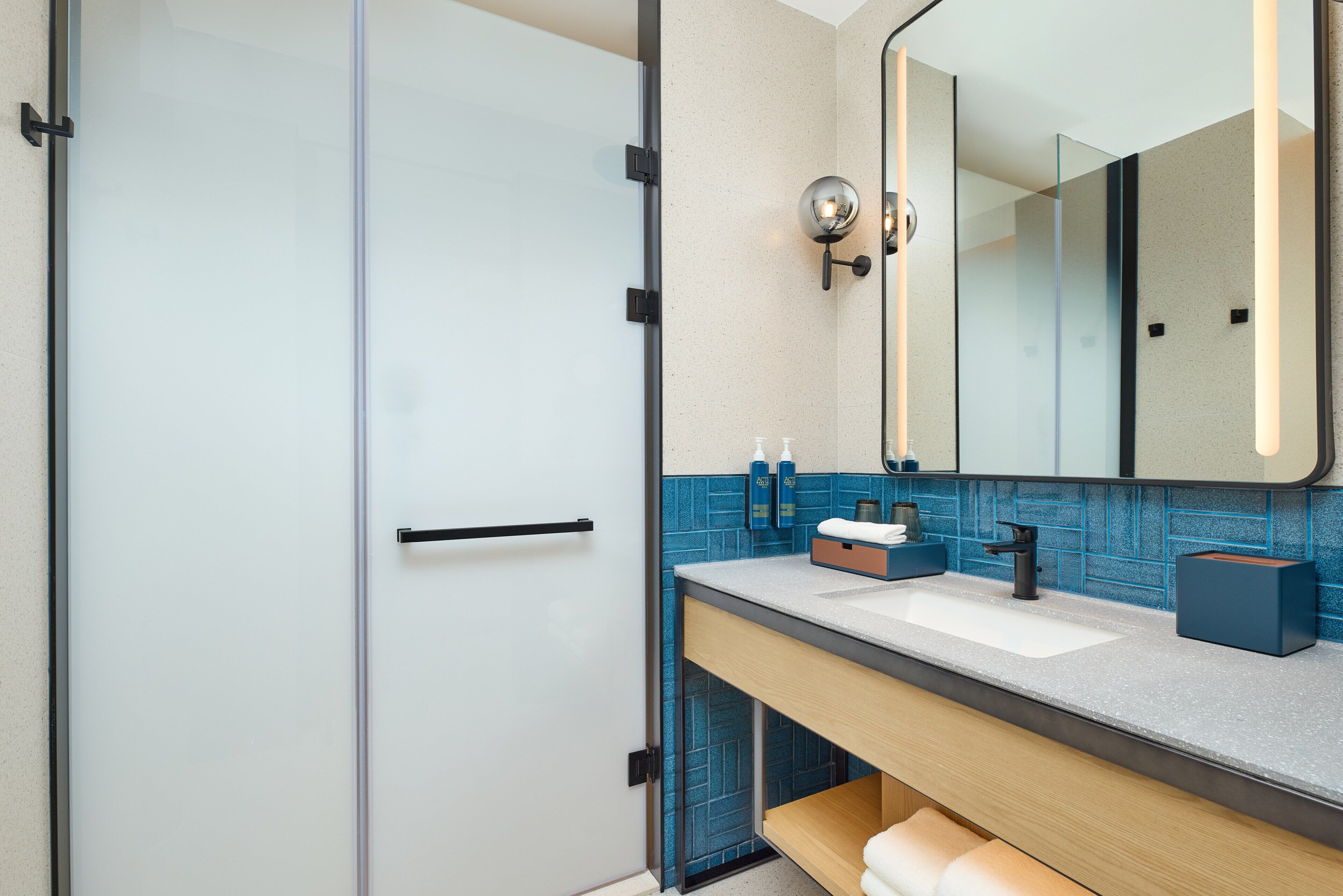 Un baño moderno con mampara de vidrio, un lavamanos con espejo y un salpicadero de azulejos azules.