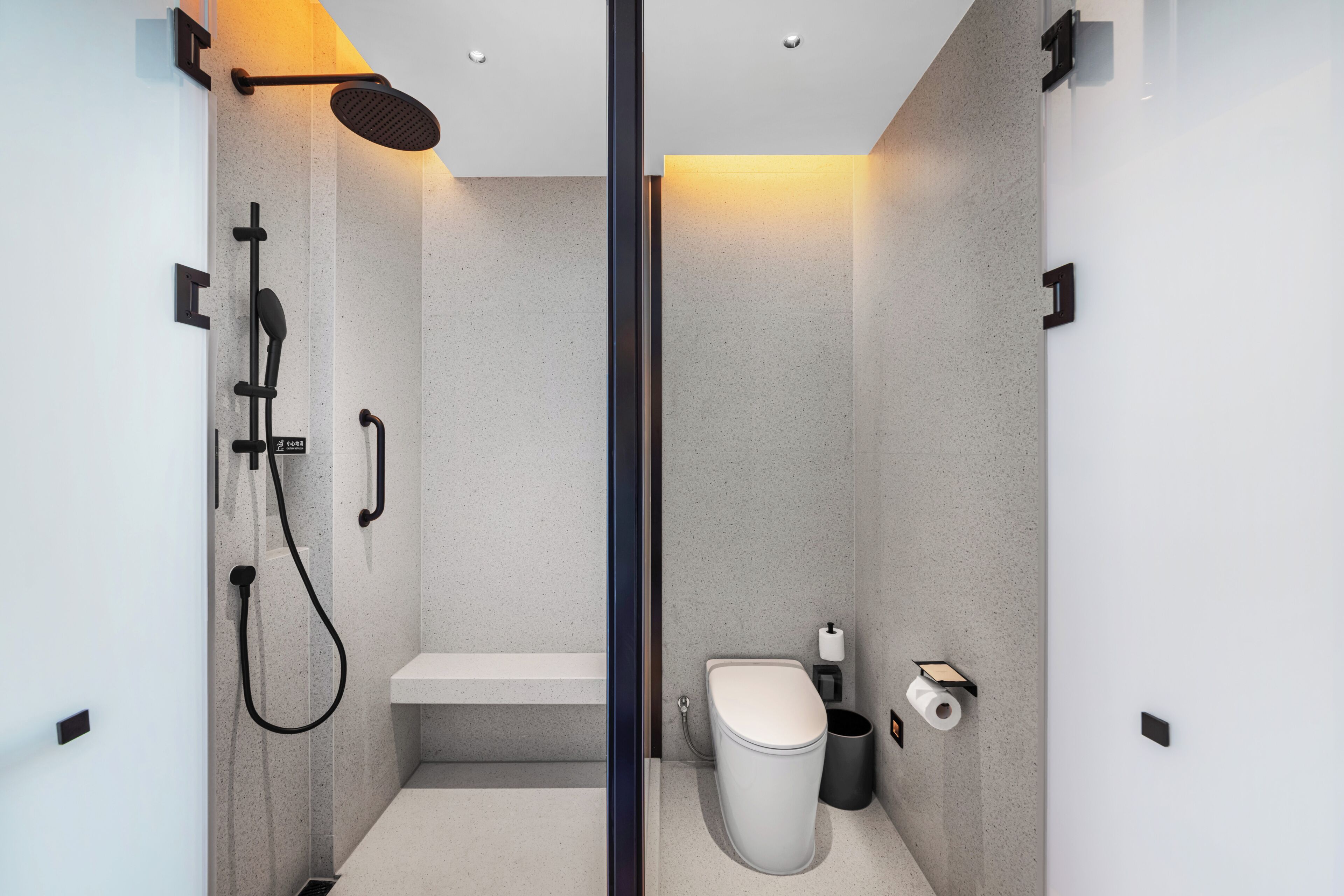 Un baño moderno con ducha, inodoro y una banca.