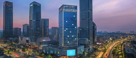 A modern cityscape with prominent skyscrapers, including a building with 'FOUR POINTS' signage, surrounded by busy roads and urban infrastructure.