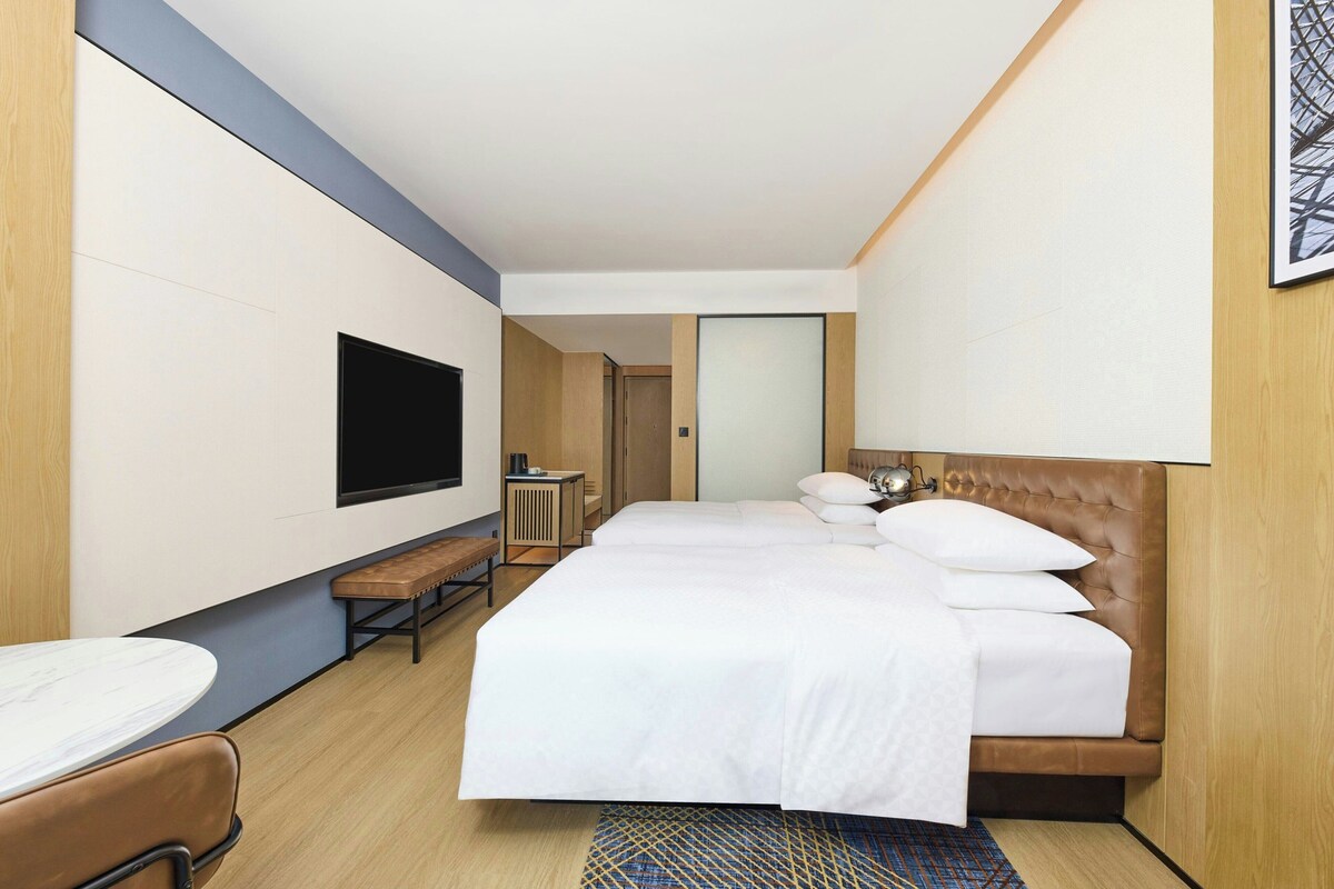 A hotel room with a bed, a TV, a bench, and a desk.