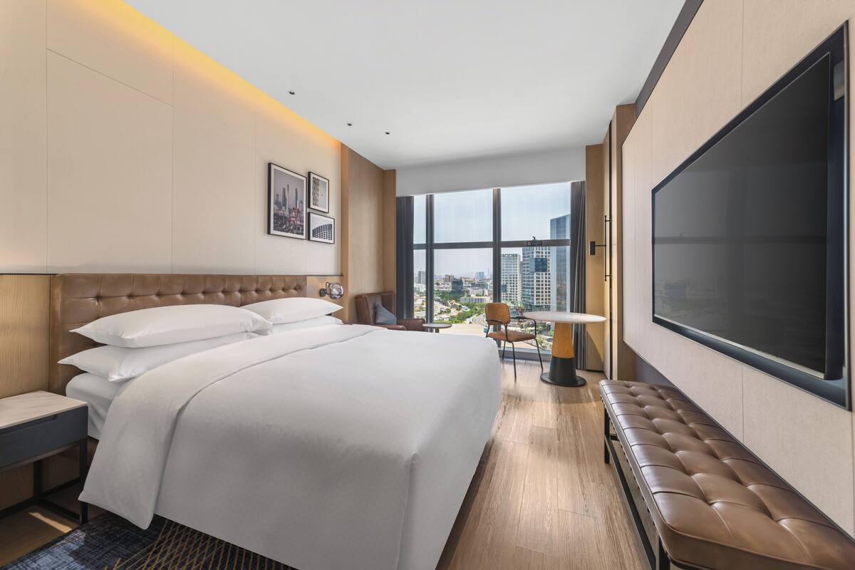 Quarto de hotel com uma cama grande, televisão, escrivaninha e vista para a cidade.