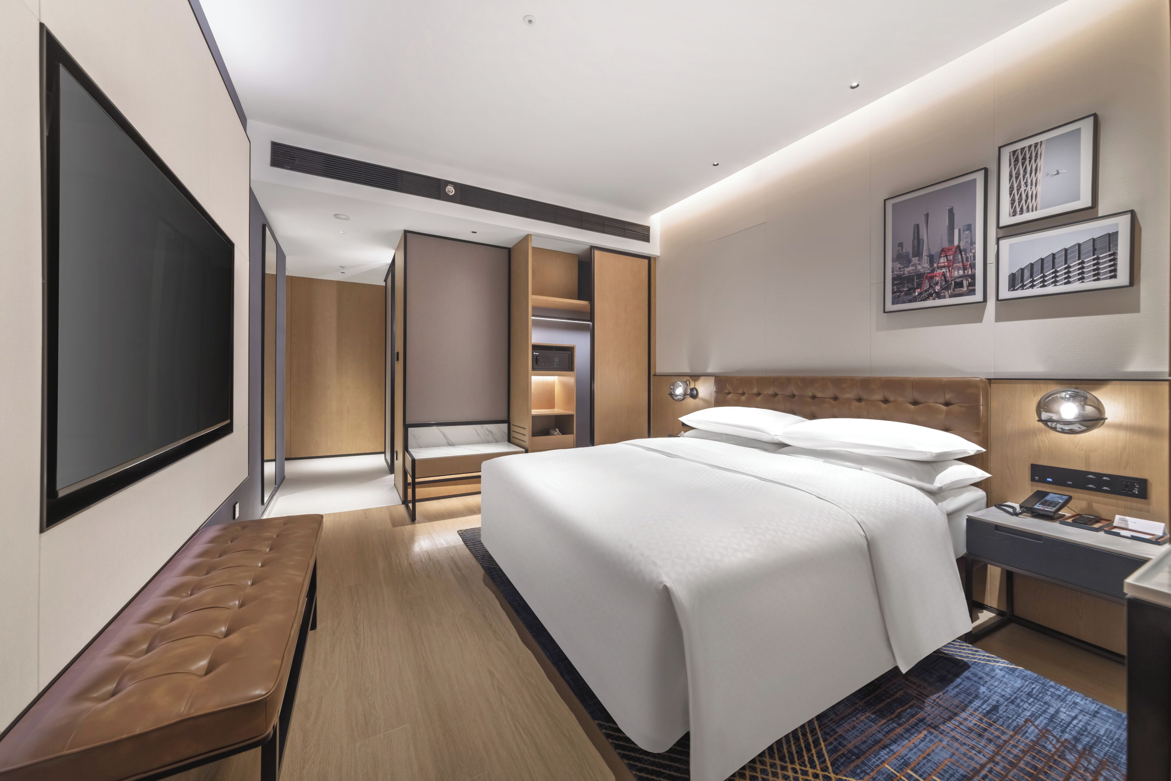 Una habitación de hotel moderna con una cama grande, un banco, un escritorio, un televisor y un armario.
