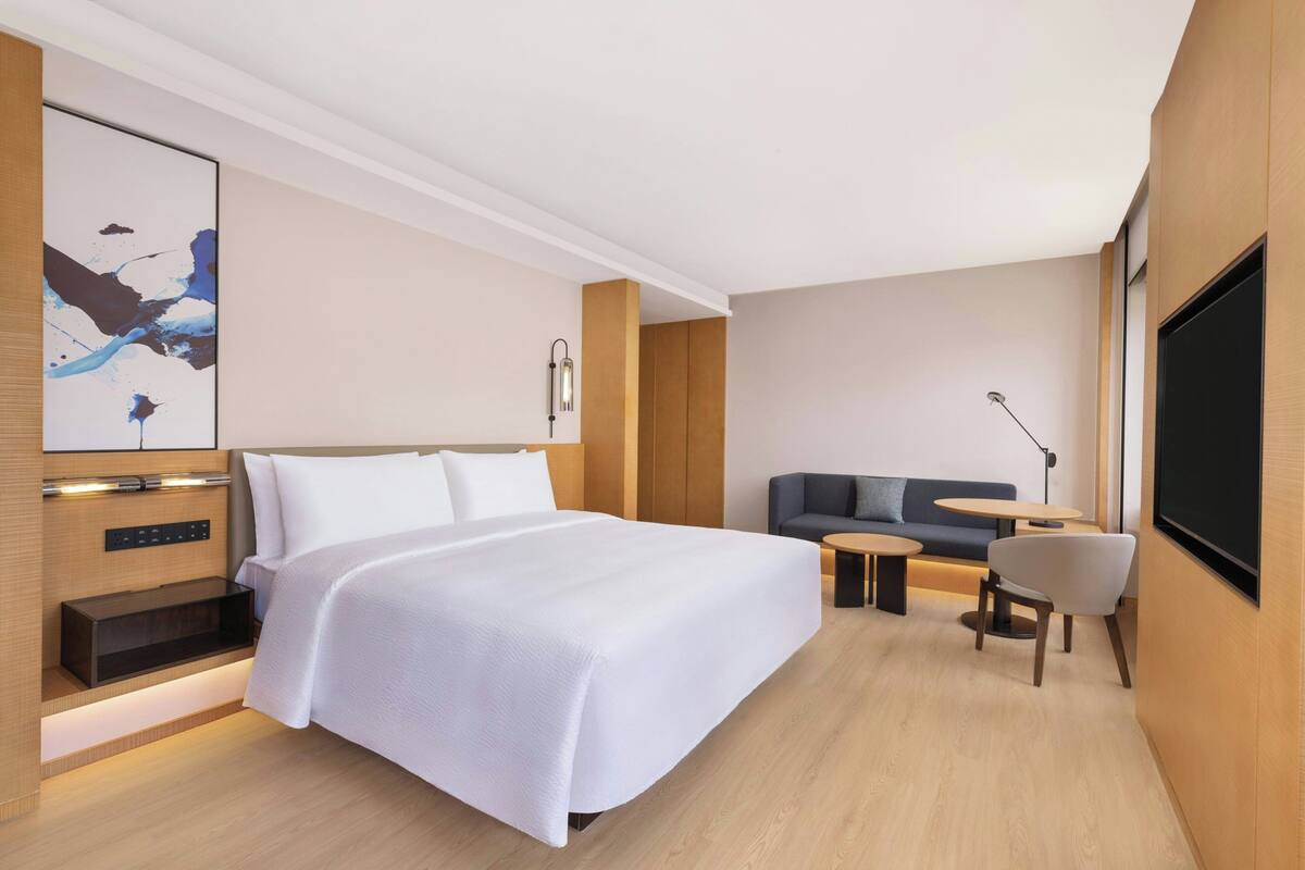 A modern hotel room with a large bed, a sofa, a small table, and a TV.