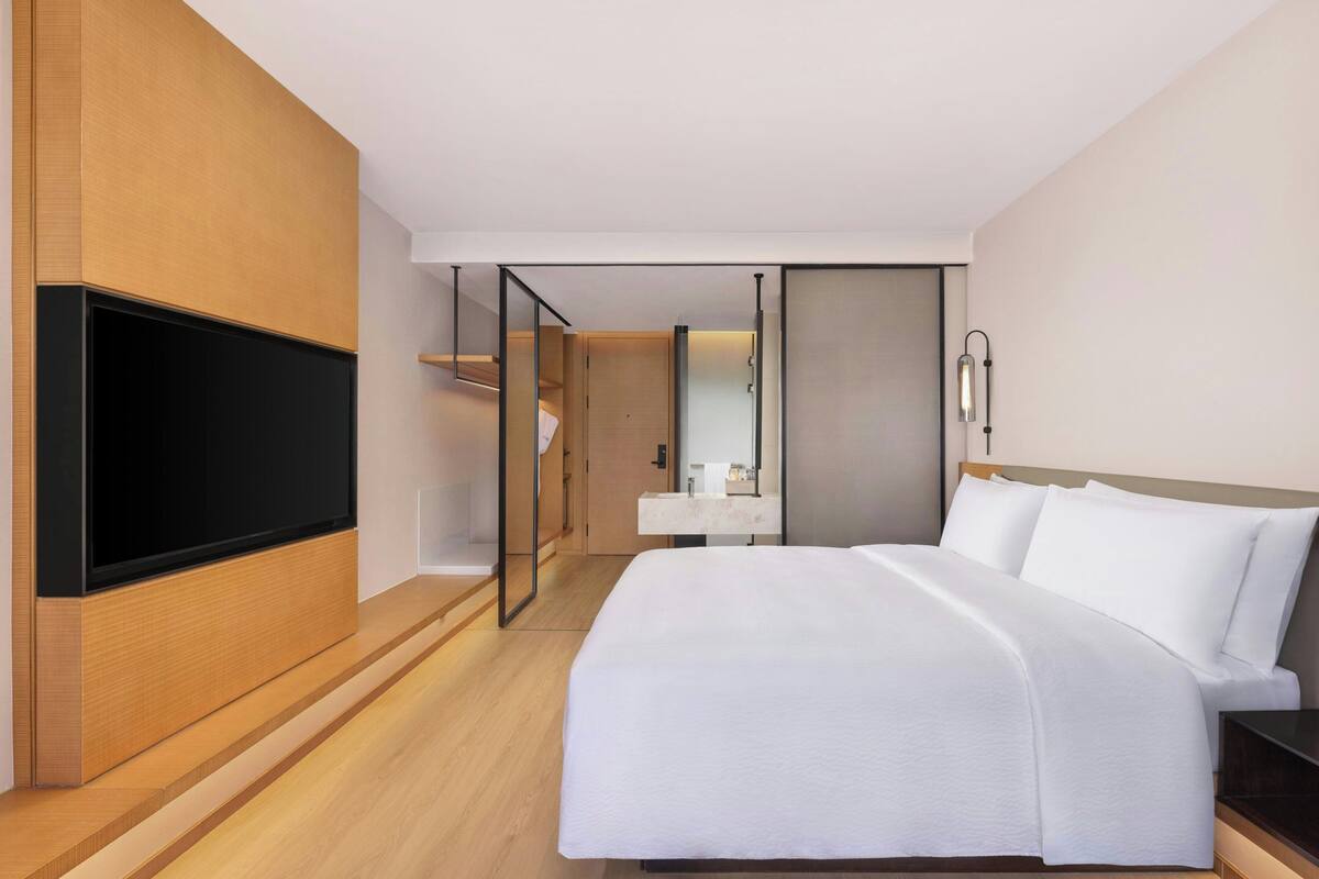 A modern hotel room with a large bed, a flat-screen TV, a bedside table, and a mirror.