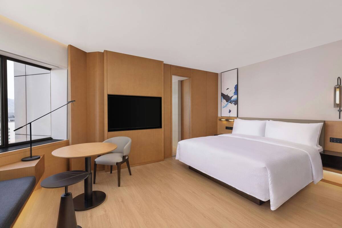 A modern hotel room with a large bed, a TV, a small table, and a chair.