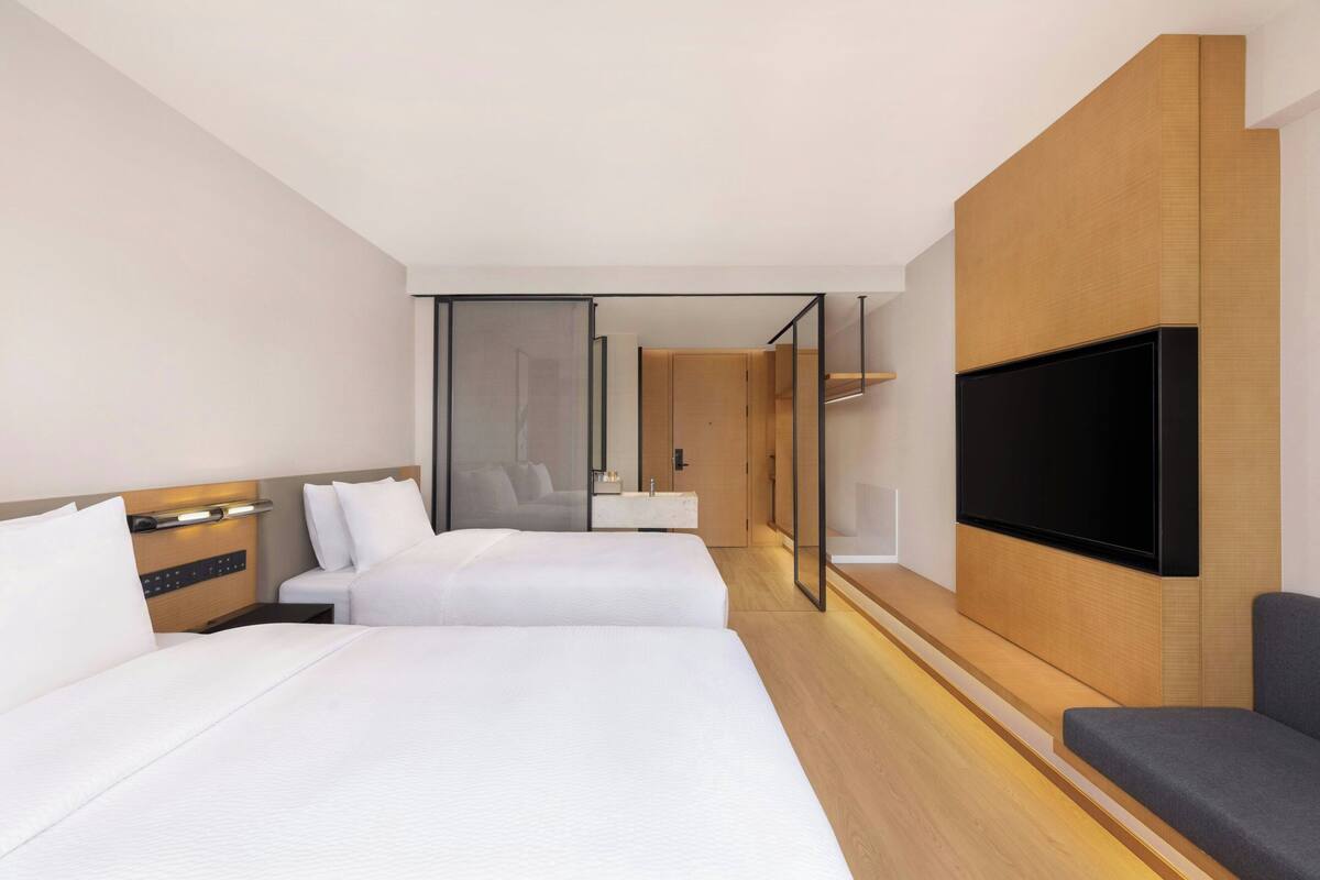 A hotel room with two beds, a TV, a sofa, and a mirror.