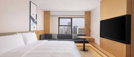 Una habitación de hotel con una cama grande, un sofá, un televisor y una ventana con vistas a la ciudad.