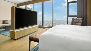 Habitación de hotel moderna con una cama grande, un televisor de pantalla plana, un rincón de descanso y vistas a la ciudad.