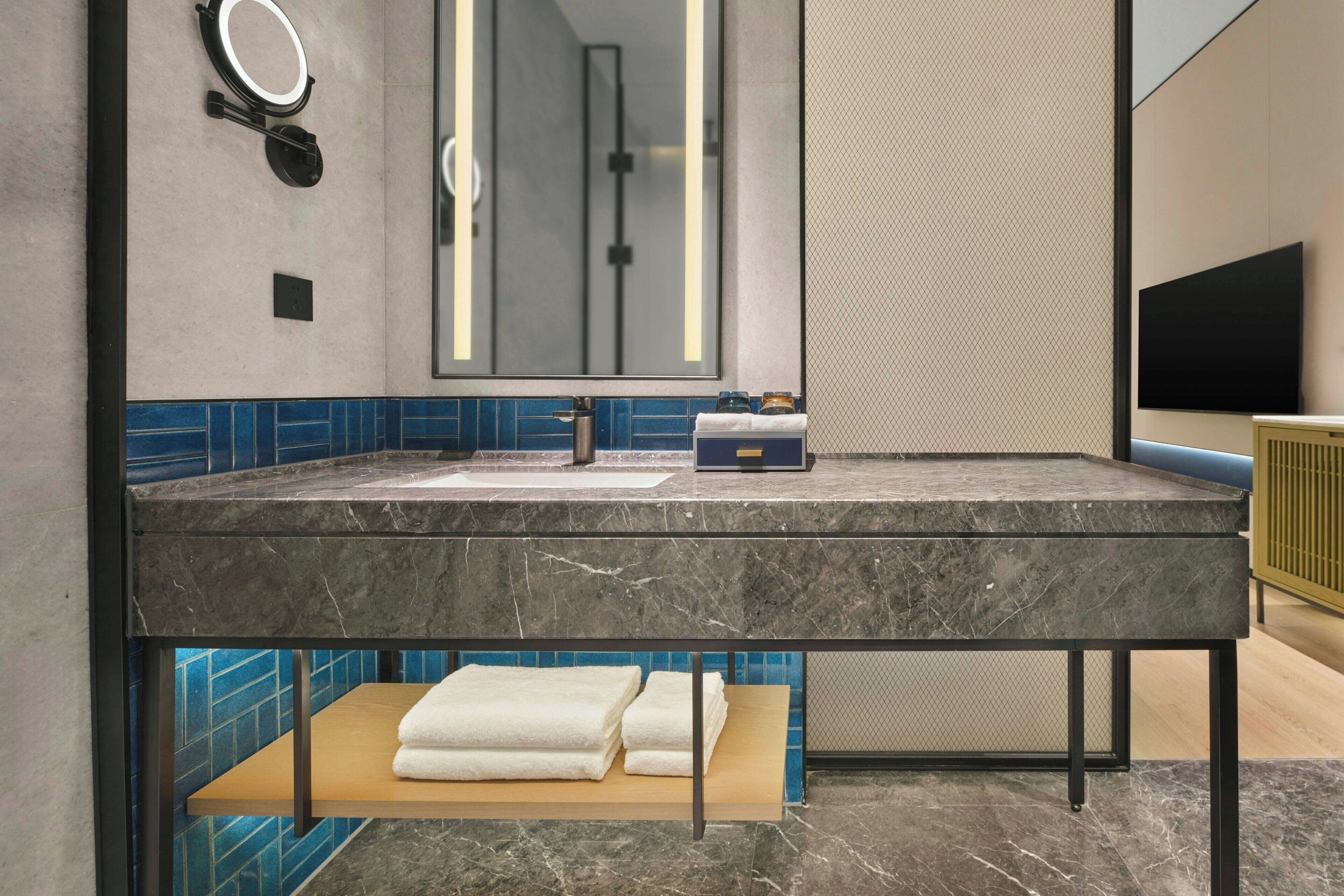 Une salle de bain avec un lavabo en marbre, un miroir, un porte-serviettes et un téléviseur.