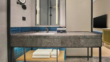 Une salle de bain avec un lavabo en marbre, un miroir, un porte-serviettes et un téléviseur.