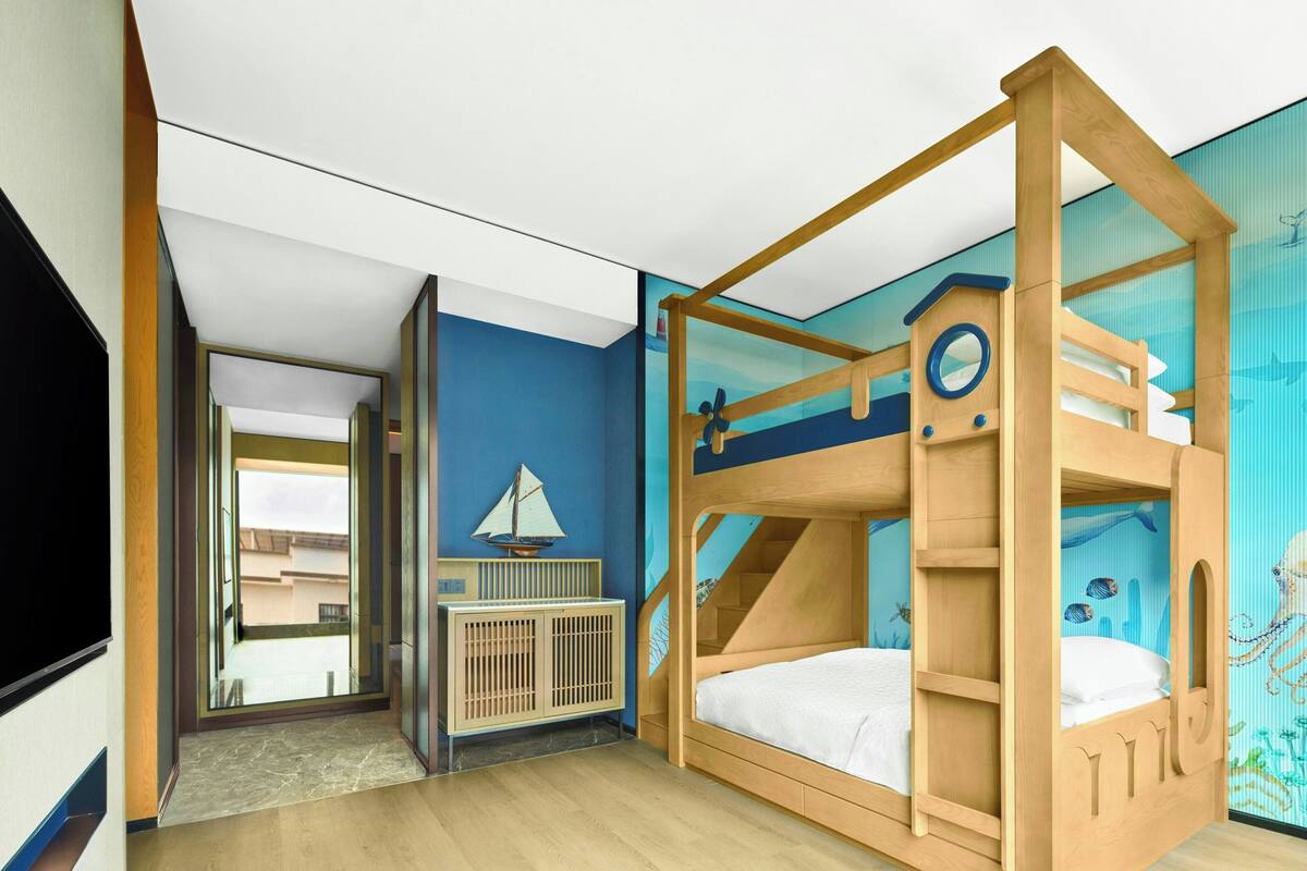 A child's room with a bunk bed, a crib, a sailboat decoration, and a mural of an underwater scene.