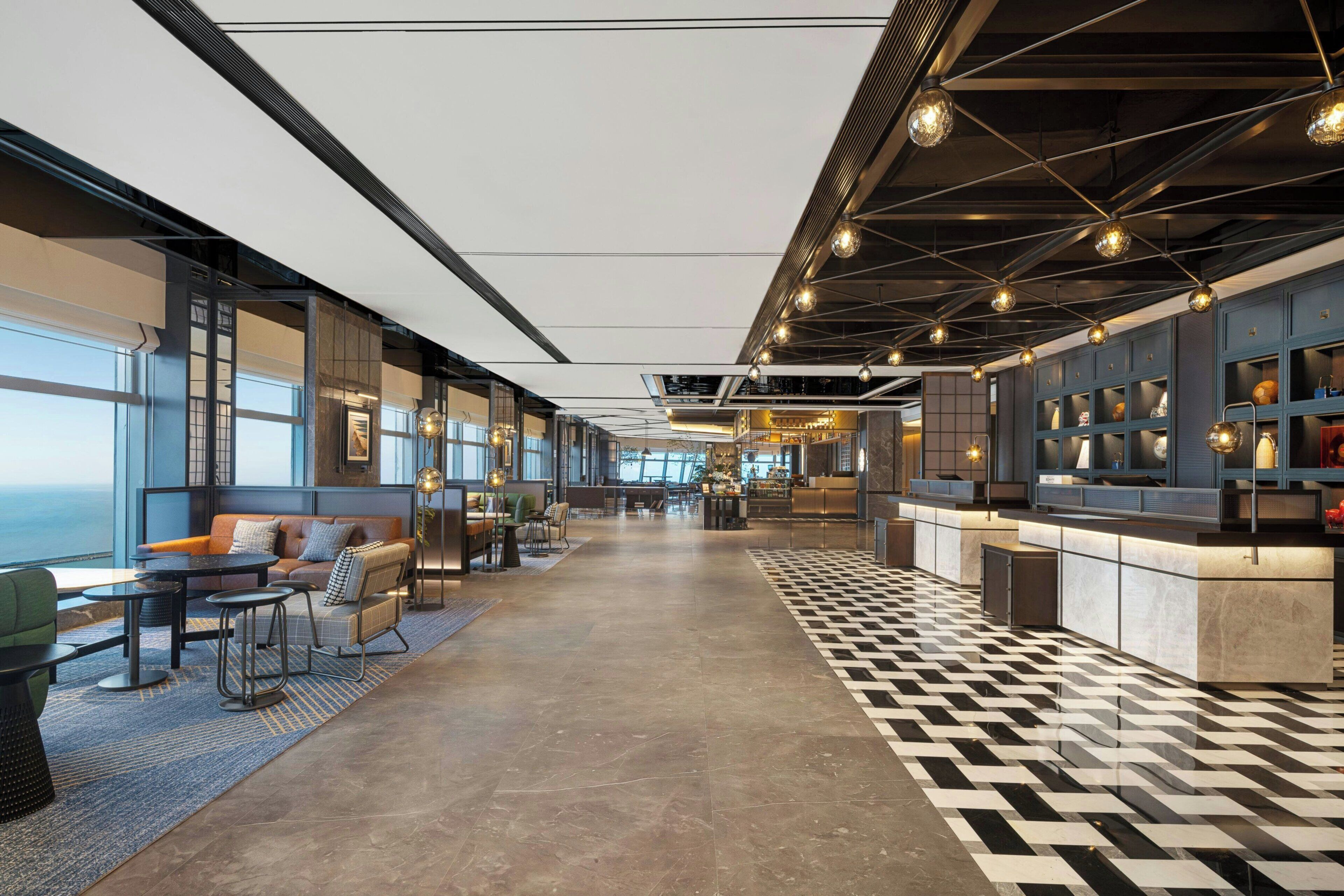 A modern hotel lobby with a checkered floor, seating areas, and a bar.