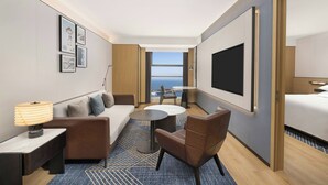 Una habitación de hotel moderna con sofá, sillón, una mesa redonda y televisión.