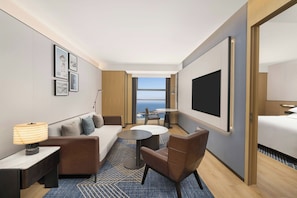 A modern hotel room with a sofa, armchair, round table, and a TV.