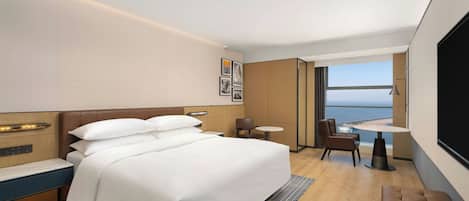 Een moderne hotelkamer met een groot bed, een klein tafeltje, een stoel en uitzicht op zee.