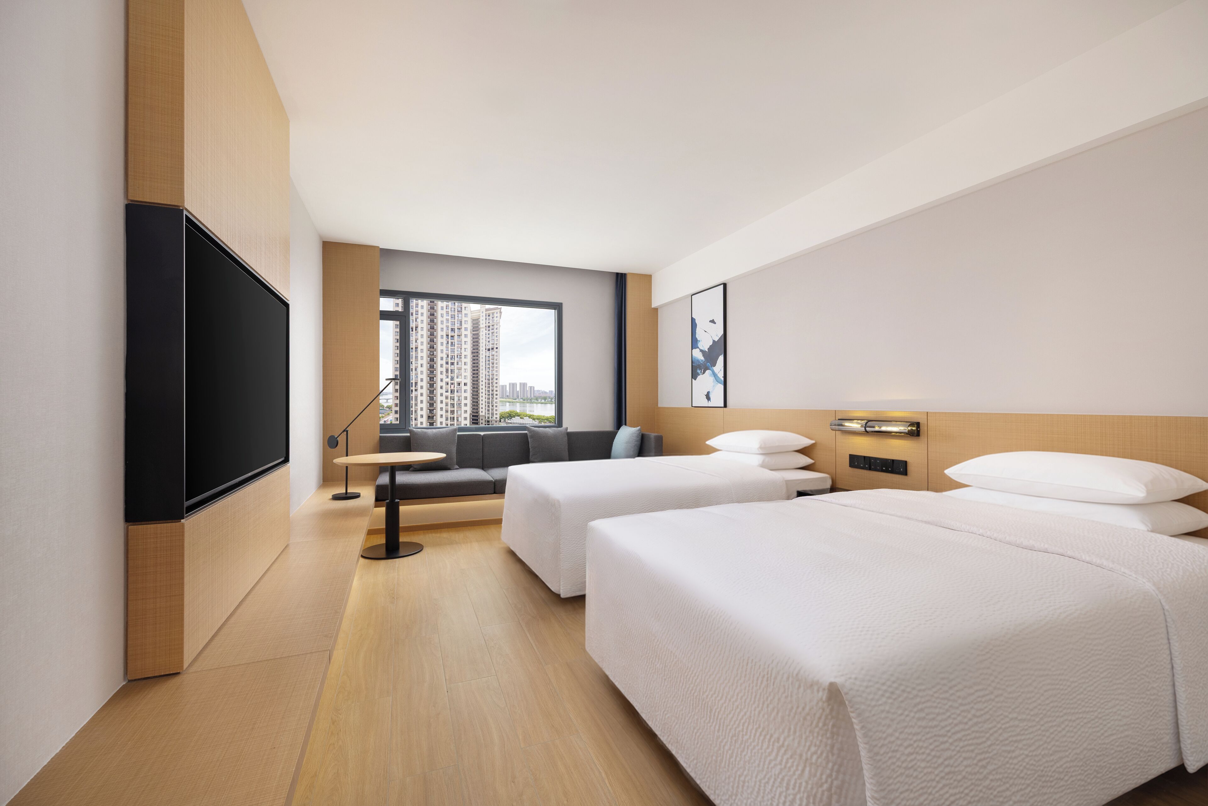 Ein Hotelzimmer mit zwei Betten, einem Sofa, einem Fernseher, einem Fenster mit Blick auf die Stadt und einem modernen Design.
