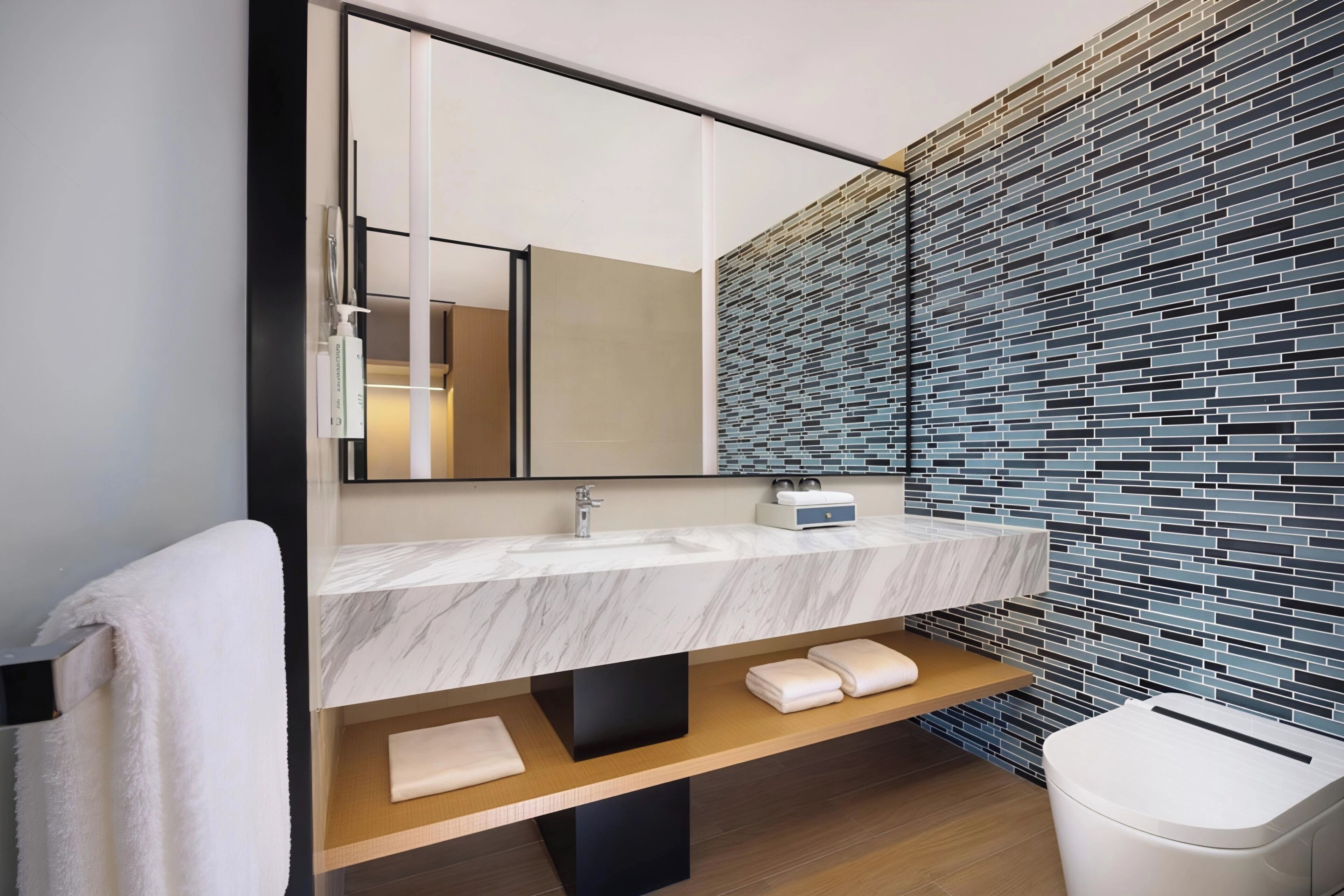 Un baño moderno con lavamanos de mármol, un espejo, pared con azulejos y estante de madera.