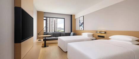 A hotel room with a large bed, a smaller bed, a sofa, a TV, and a window with a city view.