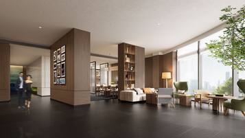 A spacious lobby with a modern design, featuring a seating area with a sofa and chairs, a bookshelf, and a large window offering a city view.