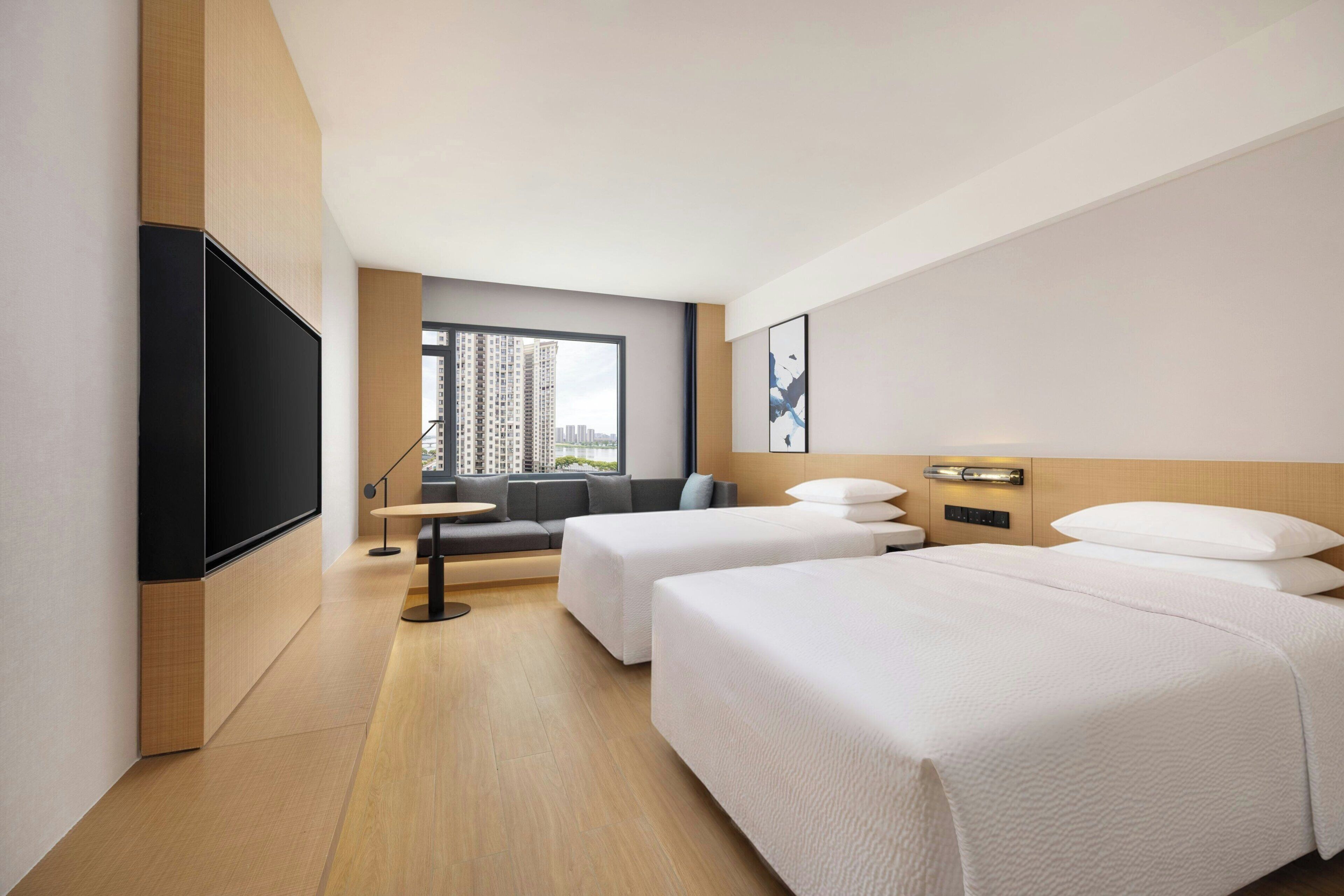 A hotel room with two beds, a sofa, a TV, and a window with a city view.
