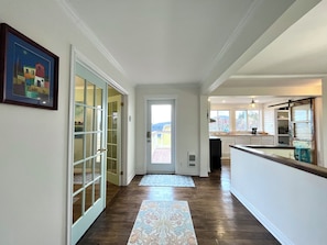 A hallway with a wooden floor, a door leading to a balcony, and a kitchen area with a window. - Stay on the Coast | Steps to EC Trails, Private Torbay Retreat | Family Friendly (Torbay)