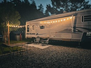 Una caravana con un porche cubierto, mobiliario exterior e iluminación con guirnaldas.