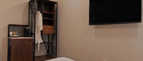 A bedroom with a bed, a TV mounted on the wall, a wardrobe, and a small table with a kettle.