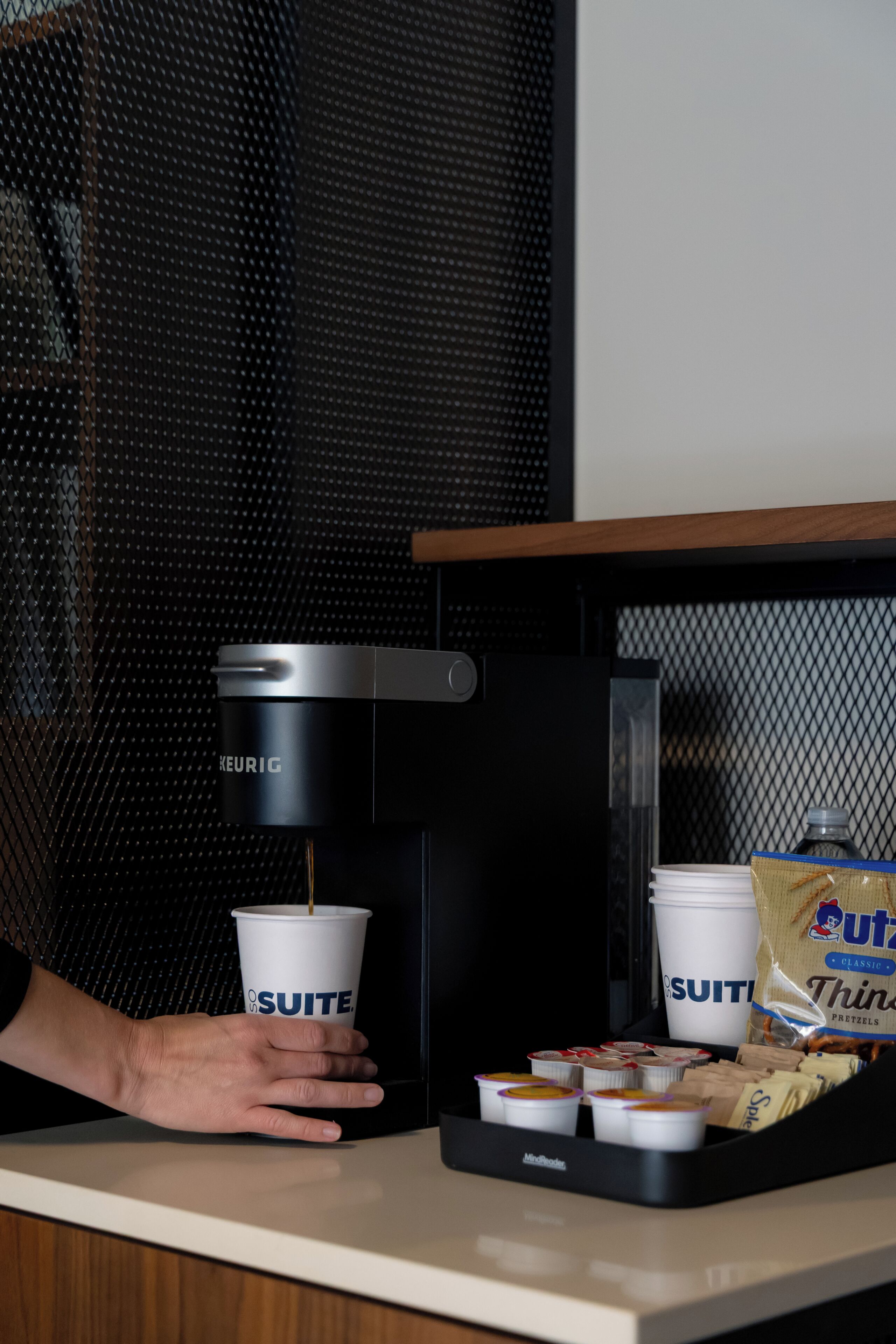 A coffee machine, cups, and snacks on a counter.