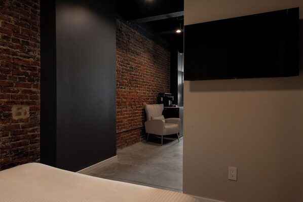 A room with a brick wall, a white chair, a flat-screen TV, and a power outlet. - The Pomerantz Hotel by Sosuite (Philadelphia)