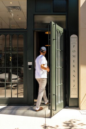 A man exiting a hotel with a glass door and a sign indicating it's a hotel by suite. - The Pomerantz Hotel by Sosuite (Philadelphia)
