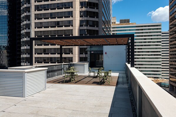 Terraço no telhado com área de estar ao ar livre, espaço coberto e vista dos edifícios altos ao redor.