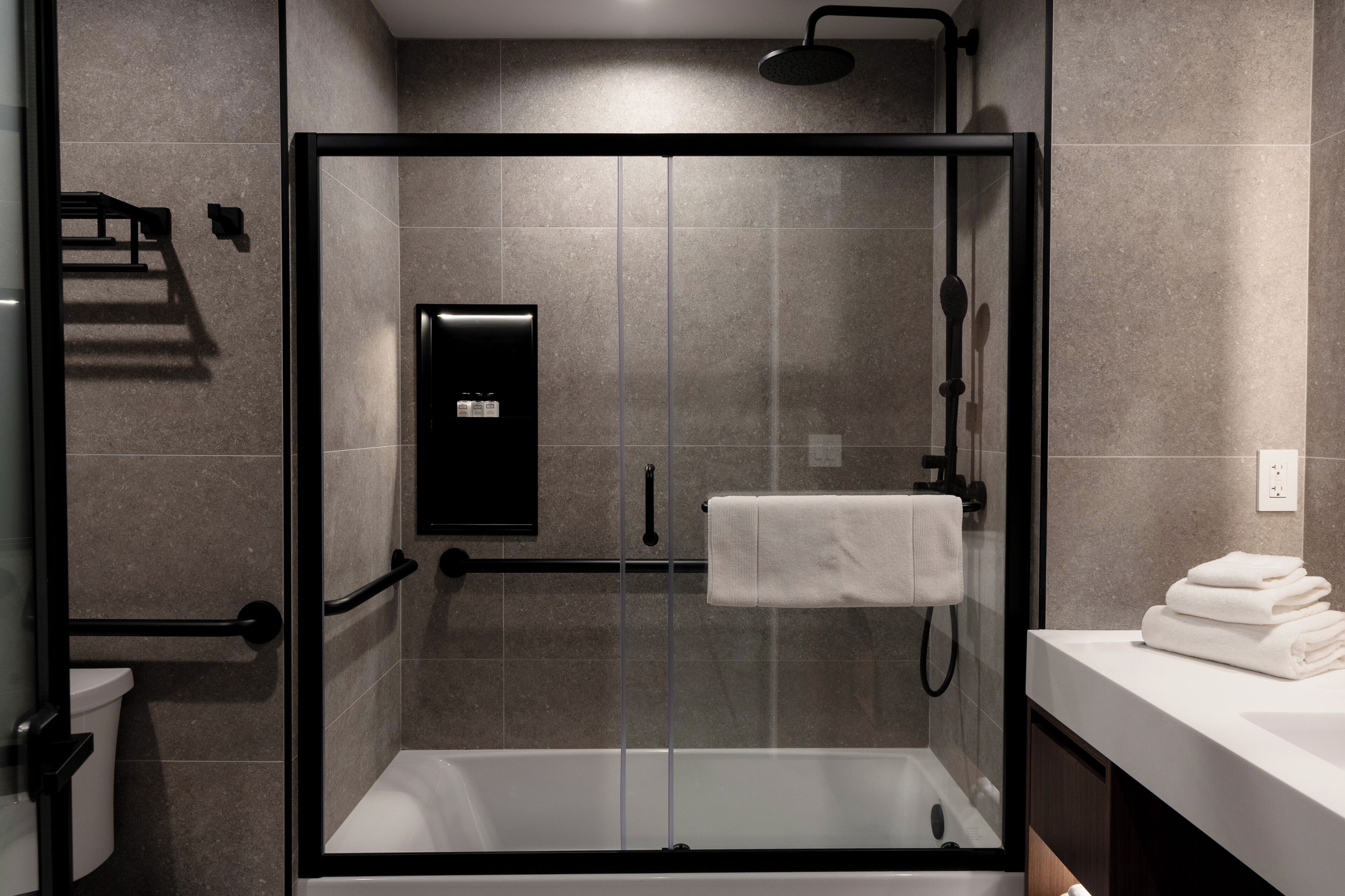 A modern bathroom with a glass-enclosed shower, a white bathtub, and a sink with a towel stack.