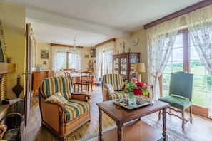 Uma sala de estar tradicional com sofá, poltronas, mesa de jantar e vista para o exterior.
