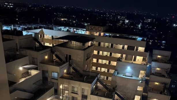 Um edifício residencial com várias andares, varandas, escadas e vista da cidade à noite.