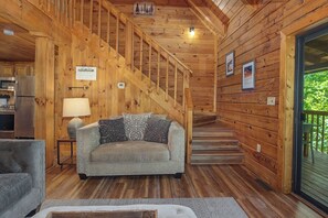 Ein Holzblockhaus-Innenraum mit einer Couch, einer Lampe, einer Treppe und einer Küchenzeile.