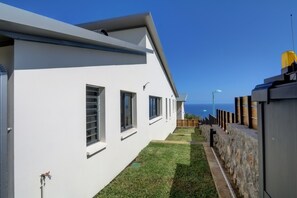 A modern building with a white exterior, a small lawn, and a stone wall. - Villa Aïna - Vue mer - Piscine (Saint-Leu)
