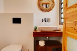 A modern bathroom with a wooden vanity, a round mirror, a white sink, and a toilet. - Villa Aïna - Vue mer - Piscine (Saint-Leu)